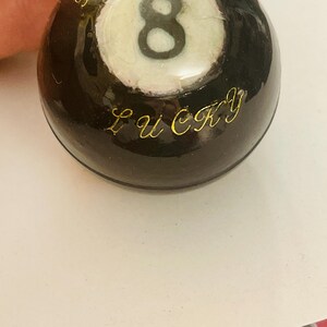 May include: A black 8-ball with a white number 8 and the word "LUCKY" inscribed in gold lettering.
