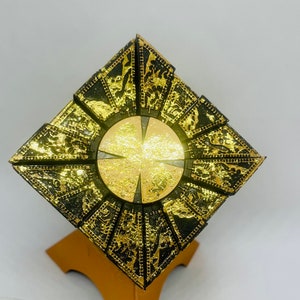 May include: A gold and black decorative puzzle box with a circular center piece. The box is made of multiple interlocking pieces and has a geometric design.