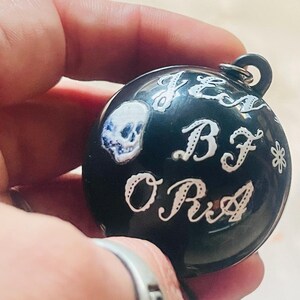 May include: Black sphere ornament with a white skull and the words "Jez BF Ora" in white cursive lettering.