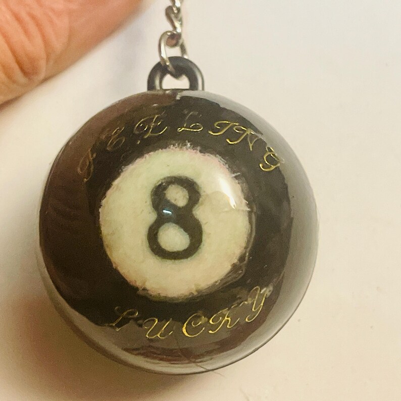 May include: A black and white 8-ball keychain with the words "The Feeling" and "Fucky" written in gold lettering.