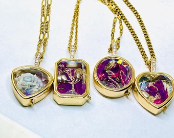May include: Four gold-toned necklaces with pendants of varying shapes: heart, circle, rectangle, and a heart shape. Each pendant features a unique design, including a carved rose and colorful, sparkling elements. The necklaces have delicate gold chains.