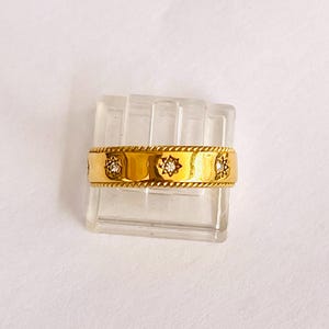 以下が含まれることがあります： 星型の模様に小さなダイヤモンドが並んだ、金のバンドリングです。