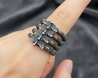 May include: A silver-toned ring with a unique design. The ring features multiple bands connected by decorative elements, creating a textured appearance. The ring is worn on a finger, showcasing its intricate details and craftsmanship.