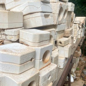 Może przedstawiać: Duża kolekcja odlewów ceramicznych z gipsu w kolorze złamanej bieli, ułożonych na powierzchni. Prostokątne i kwadratowe bloki posiadają różne formowane kształty, wgłębienia oraz wytłoczone kody alfanumeryczne, takie jak S-528 i 187B.
