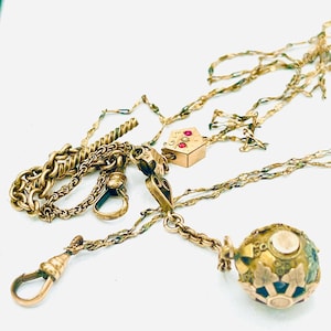 May include: An assortment of antique gold jewelry pieces, including chains, clasps, and pendants. The collection features a variety of chain styles, a small house-shaped pendant with red gemstones, and a decorative orb pendant with floral accents.