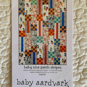May include: A white paper with a colorful quilt pattern and text. The quilt design features squares and stripes in red, orange, blue, and green. The text reads "baby nine patch stripes" and "baby aardvark".