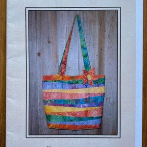 May include: A colorful striped fabric tote bag with a flower accent. The bag has a long strap and is made of a patchwork of different fabrics. The bag is labeled "String Sack" and "This & That".