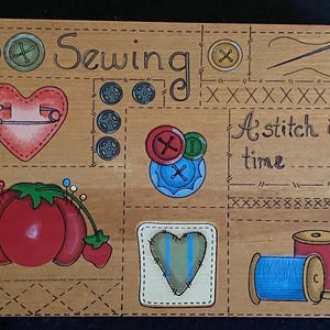 May include: A wooden sign with a painted design featuring sewing and quilting themes. The sign includes images of a sewing machine, scissors, spools of thread, buttons, and a heart with a safety pin. The text "Sewing" and "A stitch in time" are also included.