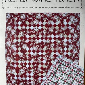 May include: A red and white floral quilt block with a nine-patch design. The block is made up of smaller squares with a floral print and a white background. The block is surrounded by a white border.