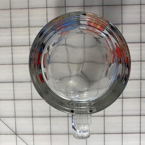 Puede incluir: Taza de cerveza de vidrio transparente con asa, vista desde abajo. La taza tiene una base gruesa y un cuerpo redondeado. El asa es acanalada y est&aacute; unida al lateral. La parte inferior de la taza tiene un patr&oacute;n texturizado.