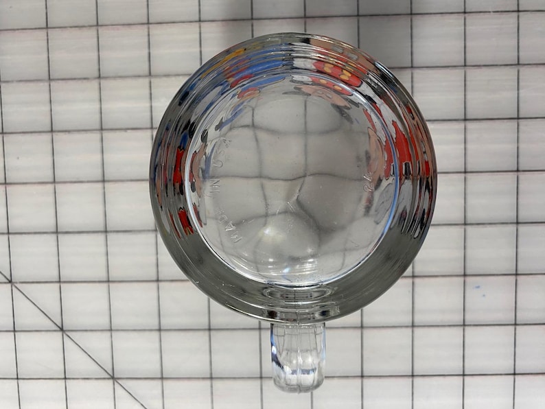 Puede incluir: Taza de cerveza de vidrio transparente con asa, vista desde abajo. La taza tiene una base gruesa y un cuerpo redondeado. El asa es acanalada y est&aacute; unida al lateral. La parte inferior de la taza tiene un patr&oacute;n texturizado.