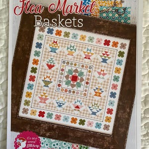 May include: A cross-stitch pattern titled "Flea Market Baskets" featuring a framed design with multiple baskets in various colors. The design includes floral accents and is set against a checkered background. The text "it's sew emma Stitchery" is also visible.
