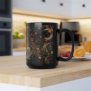 May include: Black ceramic mug with a floral pattern in shades of orange, yellow, and blue. The mug has a large handle and is sitting on a wooden surface.
