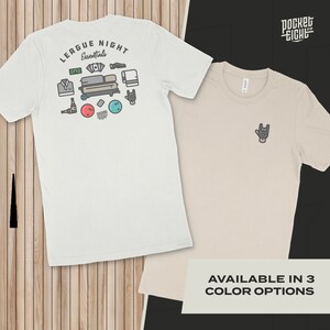 Può includere: Due t-shirt, una bianca e una beige, con un design grafico sul retro della t-shirt bianca. Il design presenta birilli da bowling, una palla da bowling, una bottiglia di birra, un portafoglio, un telefono, un asciugamano e il testo "League Night Essentials". La t-shirt beige ha un piccolo grafico di una mano che fa il segno rock and roll. Il testo "Pocket Eight Co." è nell'angolo in alto a destra dell'immagine. Il testo "AVAILABLE IN 3 COLOR OPTIONS" è nella parte inferiore dell'immagine.