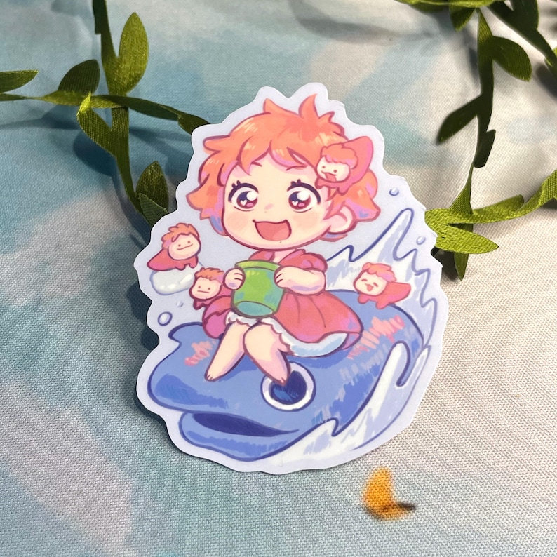 Op de afbeelding: Een sticker met een cartoonfiguur met oranje haar, die een roze jurk draagt en een groene beker vasthoudt. Het figuur zit op een blauwe walvis met witte golven eromheen. Er zijn kleinere cartoonfiguren met roze haar en rode strikjes op de walvis.