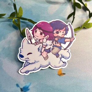 Op de afbeelding: Een sticker met een cartoonillustratie van twee mensen die op een witte wolf rijden. De vrouw heeft roze haar en draagt een bruin-witte outfit. De man heeft blauw haar en draagt een blauw-witte outfit. Hij houdt een boog en pijl vast.