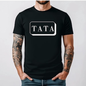 May include: Black t-shirt with the word "TATA" in a white, rectangular box. The text is in a bold, sans-serif font. The shirt is a classic crew neck style.