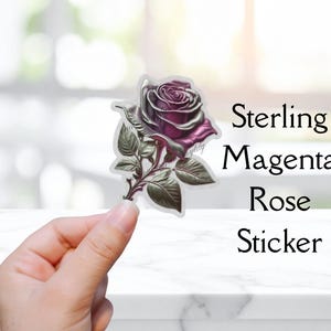 May include: A sticker featuring a detailed illustration of a sterling magenta rose. The rose has a metallic silver and magenta color scheme, with green leaves and stem. The sticker is held up by a hand. Text on the right says "Sterling Magenta Rose Sticker."