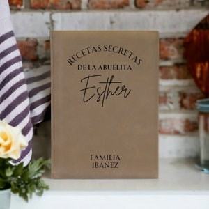 May include: A brown leather-bound recipe book with the text "RECETAS SECRETAS DE LA ABUELITA Esther FAMILIA IBAÑEZ" in black lettering.