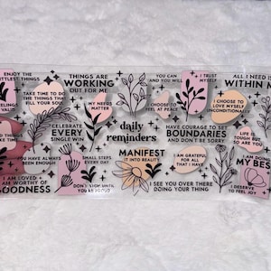 May include: Clear sticker sheet with pink and black motivational quotes and illustrations. The quotes include "Enjoy the littlest things", "Things are working out for me", "Celebrate every single win", "Daily reminders", "Manifest it into reality", "Have courage to set boundaries and don't be sorry", "I choose to love myself unconditionally", "I am doing my best", and "I deserve to feel joy".