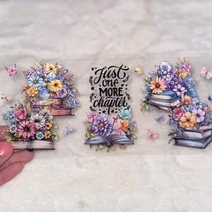 May include: Clear sticker featuring floral arrangements atop stacks of books, with butterflies. The text "Just one more chapter" is in the center. The flowers are in shades of pink, blue, yellow, and purple.