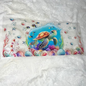 May include: A colorful sea turtle with a blue, green, and orange shell swims in a blue ocean with coral reefs and fish. The background is a white, fluffy surface.