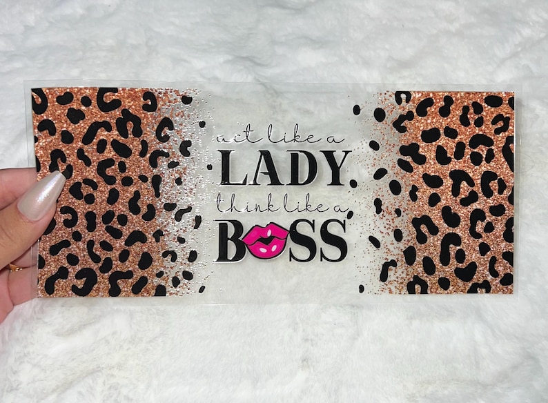 May include: A clear acrylic sign with a leopard print background and the text "act like a LADY. think like a BOSS." with a pink lipstick graphic.