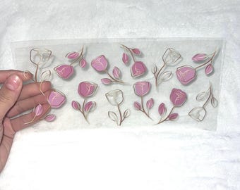 May include: A sheet of clear vinyl with pink and gold floral stickers. The stickers feature pink flowers with gold outlines and stems.
