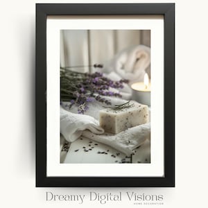 A framed digital print showing a bar of lavender soap on soft white towels with scattered lavender buds, fresh lavender stems and a glowing tealight candle in the background, displayed in a black frame on a light backdrop to evoke soothing spa decor perfect for serene bathroom wall art and botanical home styling.