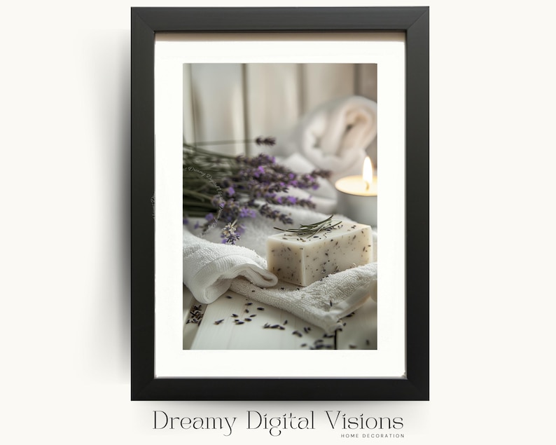 A framed digital print showing a bar of lavender soap on soft white towels with scattered lavender buds, fresh lavender stems and a glowing tealight candle in the background, displayed in a black frame on a light backdrop to evoke soothing spa decor perfect for serene bathroom wall art and botanical home styling.