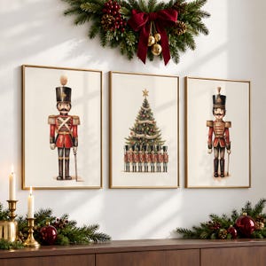 May include: A set of three framed wall art prints featuring Christmas nutcracker themes. The left and right prints display a single nutcracker in a red uniform, while the center print shows a decorated Christmas tree with a row of small nutcrackers.
