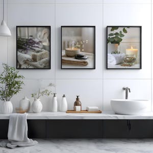 A set of three spa-themed digital art prints showing lavender soap, a steaming candle, and eucalyptus with a candle, hung in a modern white bathroom styled with minimalist ceramics and plants to enhance a calming decor scheme.