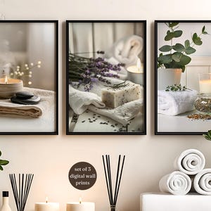 A digital illustration of a spa-themed trio featuring a steaming candle, lavender soap, and a eucalyptus candle scene, displayed in black frames above a shelf styled with rolled towels, candles, reed diffusers, and green plants to create a calming, neutral bathroom decor atmosphere suitable for zen spa wall art.