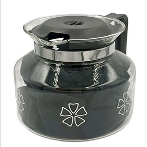May include: A clear glass coffee pot with a black lid and a silver band around the top. The pot has a black floral design on the bottom.
