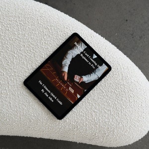 May include: A black tablet displaying a book cover titled "Black Card Counting 101: Beginner to Pro" by Jim Allen. The tablet rests on a white, textured, curved surface against a gray background.