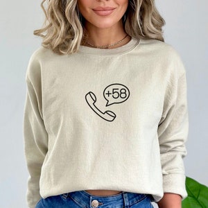 May include: A beige sweatshirt with a black phone icon and a speech bubble that says +58.