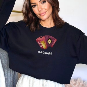 May include: A black cropped sweatshirt with a red and gold accordion illustration and the text "Del Carajo!" printed on the front.