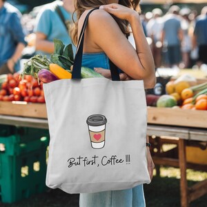 Puede incluir: Una bolsa de tela blanca con asas negras y un gráfico de una taza de café con un corazón rojo. El texto "But first, Coffee!!!" está impreso en la bolsa.