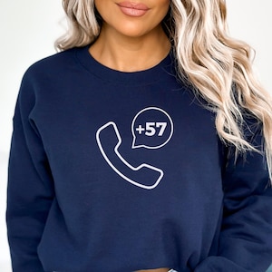 以下が含まれることがあります： 白い電話のアウトラインと「+57」というテキストの吹き出しがついた、ネイビーブルーのクロップドスウェットシャツです。