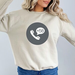 May include: A beige sweatshirt with a grey circle graphic featuring a white phone icon and a speech bubble with the text "+58".
