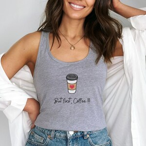 Puede incluir: Camiseta de tirantes gris con un gráfico de una taza de café con un corazón y el texto "But first, Coffee!!!".