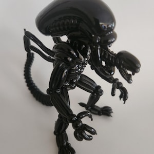 May include: A glossy black figurine of an Alien creature, featuring a large, smooth head, elongated body, and a segmented tail. The figure has detailed skeletal features and articulated limbs, showcasing a menacing pose. This collectible item is a representation of the iconic movie monster.