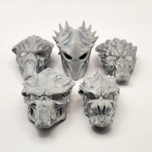 Peut inclure: Cinq masques de Predator imprimés en 3D de couleur grise. Les masques sont détaillés et présentent une variété de motifs.