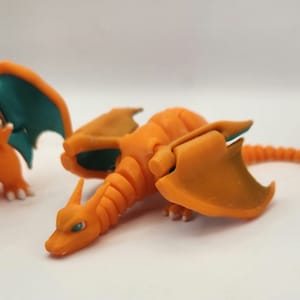 May include: Orange and teal articulated plastic toy dragon with wings and a tail. The dragon is posed with its head down and its wings spread out.