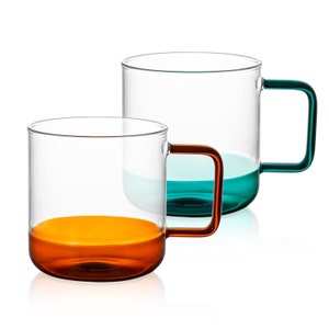 May include: Two glass mugs with coloured bottoms. One mug has a teal bottom and the other has an orange bottom.