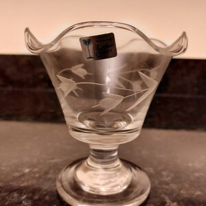 May include: A clear glass dessert dish with a scalloped rim and a pedestal base. The dish features etched floral designs and a sticker that reads "Handcut in England,  Cormon Glass."