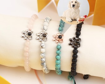 May include: Four beaded bracelets in pink, white, turquoise, and black. Each bracelet features a flower-shaped charm with a black center. A dog wearing a party hat is in the background.