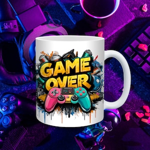 May include: White ceramic mug with a colorful graphic design featuring a video game controller and the words "GAME OVER".