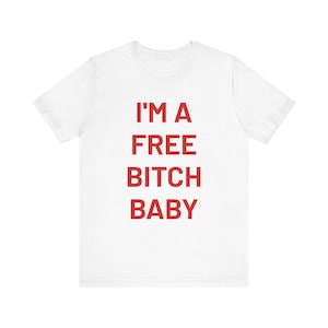 Op de afbeelding: Wit t-shirt met de rode tekst "I'M A FREE BITCH BABY" in een vetgedrukte, schreefloze letter. Het t-shirt heeft korte mouwen en een ronde hals. De tekst staat gecentreerd op de voorkant van het shirt.