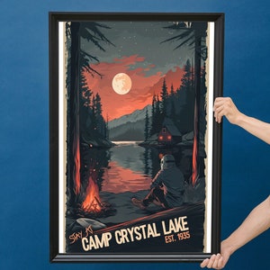 May include: A framed poster with a retro design featuring a dark silhouette of a person sitting by a campfire in front of a lake. The lake is surrounded by trees and mountains. The moon is full and red in the sky. The poster reads "Stay at Camp Crystal Lake Est. 1935".